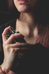 Black glass bottle with fragrance in woman hands, sprinkling toilet water on her neck, testing...