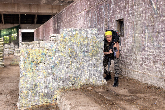 Strong woman with riffle on hands and backpack play hide and seek in old industrial place