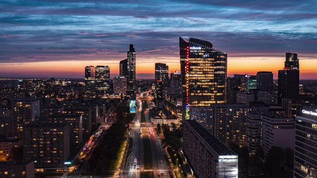 Fly forwards above wide downtown boulevard. Amazing hyperlapse of straight multilane main road leading between modern skyscrapers against sunset sky. Warsaw, Poland