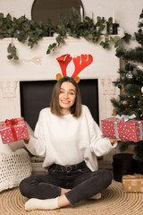 A surprised young girl sits and holds two red Christmas gifts near the white fireplace