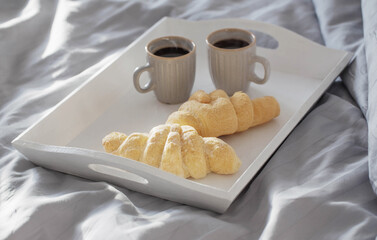 two croissants and two cups of coffee on  bed