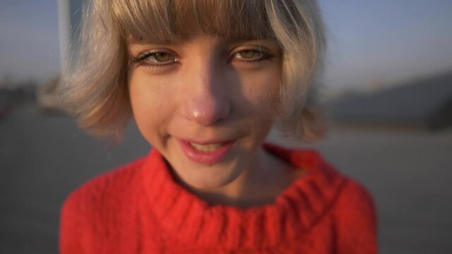 close up outdoor portrait of funny pretty teenage blond girl, smiling in a silly way, grimacing, urban girl portrait