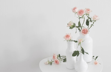pink roses in white vase on  table on background white wall