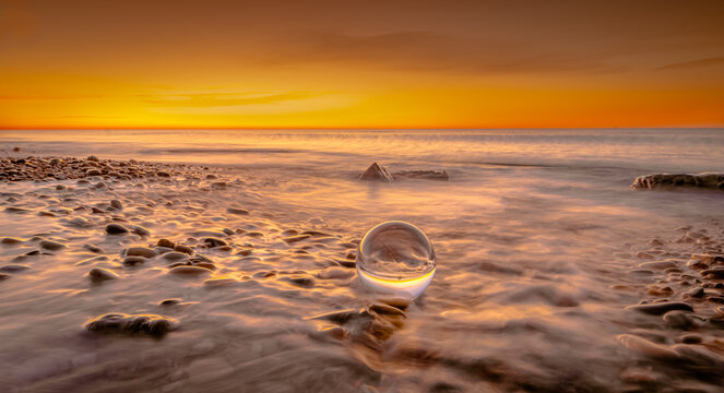 Boule de cristal sur des galets d'une plage au lever de soleil. © ODIN Daniel