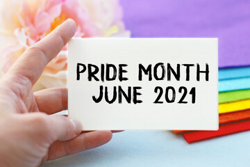 A woman's hand holds a piece of paper with the inscription INTERSEX AWARENESS DAY, against the background of a stack of cloth folded in the colors of the LGBT flag. LGBT concept.