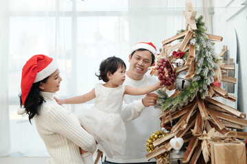 Happy family of mother, father and little daughter decorating Christmas tree together