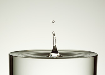 drop of water splashes into glass on bright background 