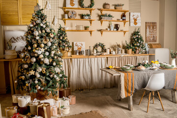 Interior of minimalistic kitchen with white walls, white floor, white countertops. Kitchen with white furniture. Kitchen decorated with garlands and Christmas toys. Christmas tree upside down.