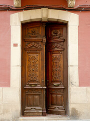 Classical double door made of warm red wood in Jaca, Huesca, Spain. Vintage entrance, classy antique details, floral curvy ornament