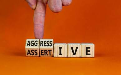 Aggressive or assertive symbol. Businessman turns wooden cubes, changes the word Aggressive to Assertive. Beautiful orange background, copy space. Business, psychological aggressive assertive concept.