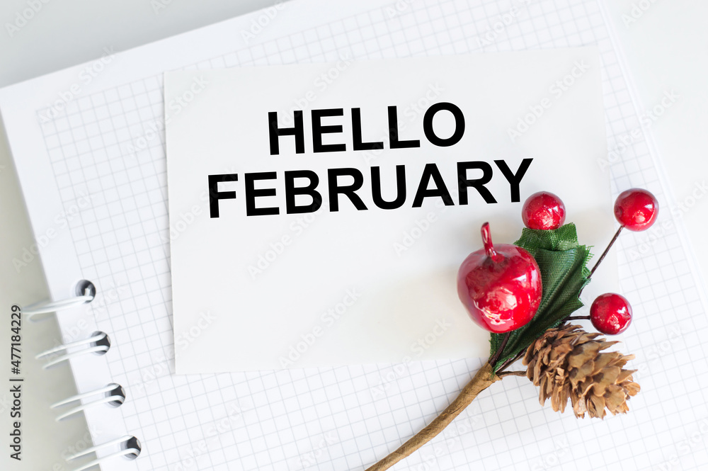 Poster hello february greeting card, text on a white card with a notepad on the table