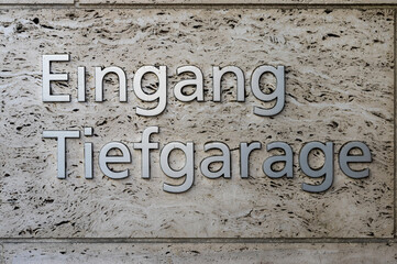 Schriftzug, Schild „Eingang Tiefgarage“ aus silbernen, verchromten Buchstaben auf einer Wand aus Travertin in Nahaufnahme