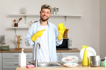 Handsome young man pointing at cleaning sponge in kitchen