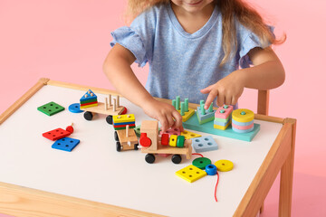 Cute little girl playing with building blocks at table on pink background