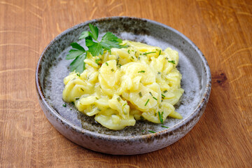 Traditioneller deutscher Kartoffelsalat mit Zwiebel und Schnittlauch serviert als close-up in einer Design Schale auf einem Design Holz Board