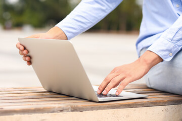 Fototapeta premium Young man using laptop on bench outdoors, closeup