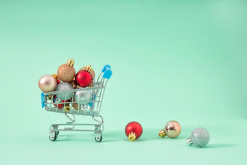 Creative Christmas shopping cart full of New Year decoration balls concept in pastel mint background. Winter is coming.