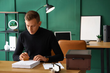 Young male notary public attaching seal to documents in office