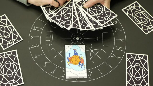 Adult woman opens and puts tarot card. Hands of fortune teller woman open and shows THE WHEEL OF FORTUNE card on table with altar of tarot. Forecasting concept.