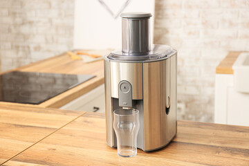 Modern juicer with glass on table in kitchen