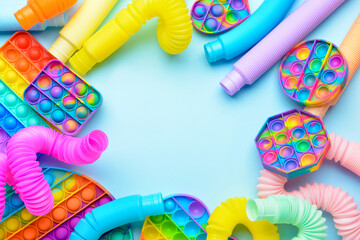 Frame made of colorful Pop Tubes and Pop it fidget toys on blue background