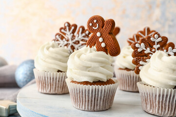 Wooden board of tasty Christmas cupcakes with gingerbread cookies on table, closeup