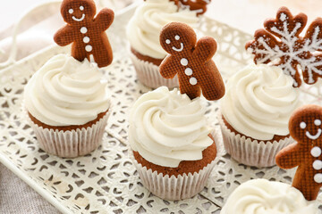 Tray of tasty Christmas cupcakes with gingerbread cookies on light background, closeup