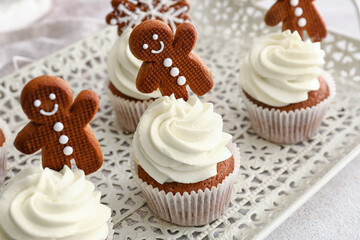 Tray of tasty Christmas cupcakes with gingerbread cookies on light background, closeup