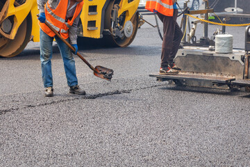 Road workers pave fresh asphalt using a shovel, paver and vibratory roller. - obrazy, fototapety, plakaty
