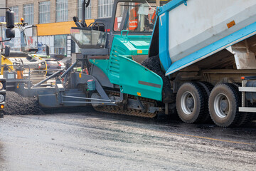 Fototapeta na wymiar Construction of a new road, a truck pours hot asphalt into the bucket of an asphalt paver. Close-up.