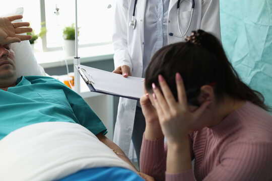 Doctor holding documents in front of crying wife and patient in hospital room