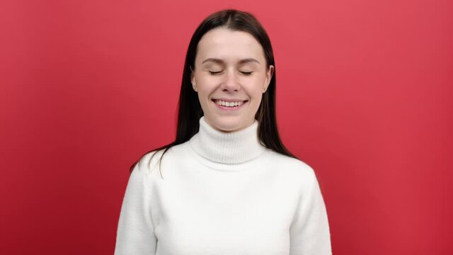 Portrait of fun young woman looking cross eyed with stupid dumb face, brunette girl having awkward confused comical expression, wears knitted sweater, posing isolated over red color background studio
