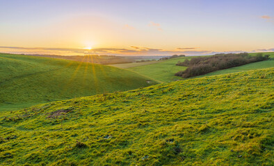 a golden sunset, low illuminated cloud on the horizon over a deep green grass valley, North Wessex...