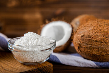 Coconut flakes in a bowl, coconuts on a wooden background. Close-up.