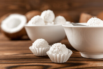 coconut candies in a bowl, coconuts on a wooden background. Close-up.