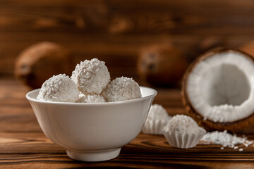 coconut candies in a bowl, coconuts on a wooden background. Close-up.
