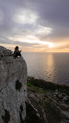 Sad girl sitting on the cliff, writing someone on her phone dingli window