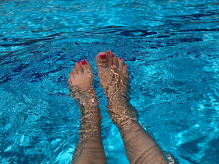 Beautiful women legs in blue water. Beautiful female feet relaxing by the swimming pool. Summer...