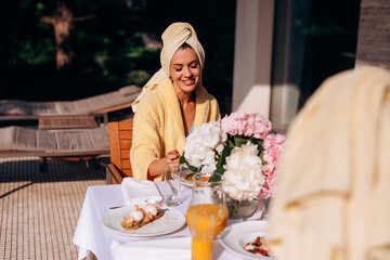 Young smiling woman in a Bathrobe and towel on head having breakfast in hotel