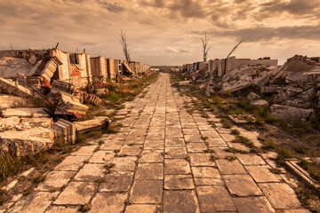 Path between demolished buildings with expressive sky and dry trees. Abandoned public Cemetery in...