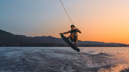 latino mas doing wakeboarding in a lake with mountains in the background - obrazy, fototapety, plakaty