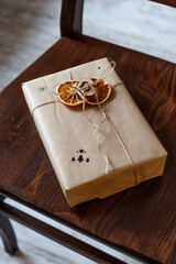 Zero waste Christmas gift in craft paper on rustic brown chair with oranges slices. Plastic free sustainable lifestyle