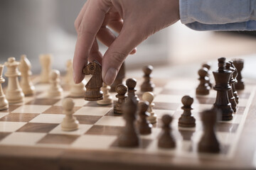 Chess game in action. The player a young girl performs a move of a chess piece horse figure for a game of chess horse soars in the air. Wooden brown checkerboard.
