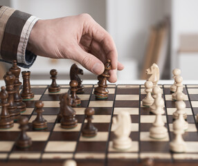 Chess game. The player in the shirt makes a move. Hand-sleeved shirt in a cage take on a wooden figure. Execution of a move with the right hand. Chess piece ferz officer.
