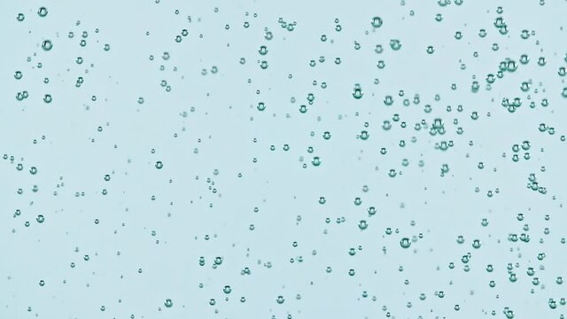 Macro shot of air bubbles in water rising up on light blue background. Slow motion. High quality FullHD footage