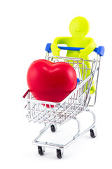 Green toy abstract man with smile hold shopping trolley with big red heart inside isolated on white background. Concept ideas for health care, shopping in pharmacies or supermarket sales