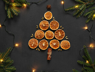 dried orange slices lai in the form of christmas tree on a board with anise stars, cinnamon sticks, fir tree branches, top view