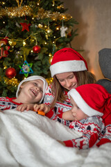 three children have fun on the background of the Christmas tree. children are dressed in New Year's pajamas and santa hats. selektiver fokus
