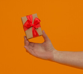 gift box with red ribbon in hand on yellow background, close-up