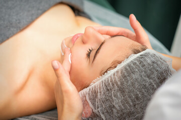 Fototapeta na wymiar Spa facial skincare. Close-up of a young caucasian woman getting spa moisturizing face massage treatment at beauty spa salon